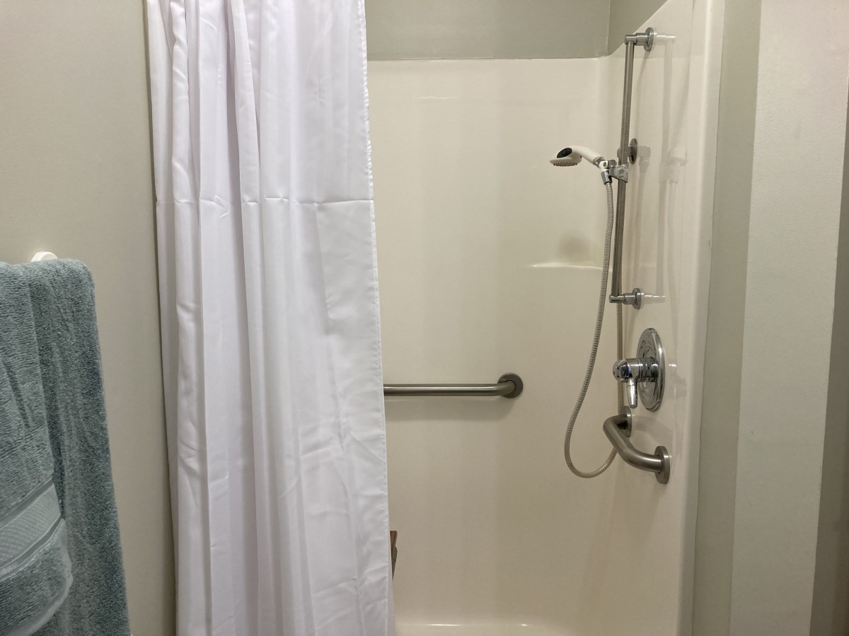 A bathroom shower with a white curtain and grab bar.