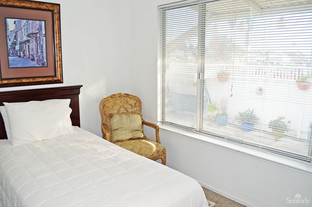 A cozy bedroom featuring a bed with white linens, an upholstered chair by the window, and a bright atmosphere.