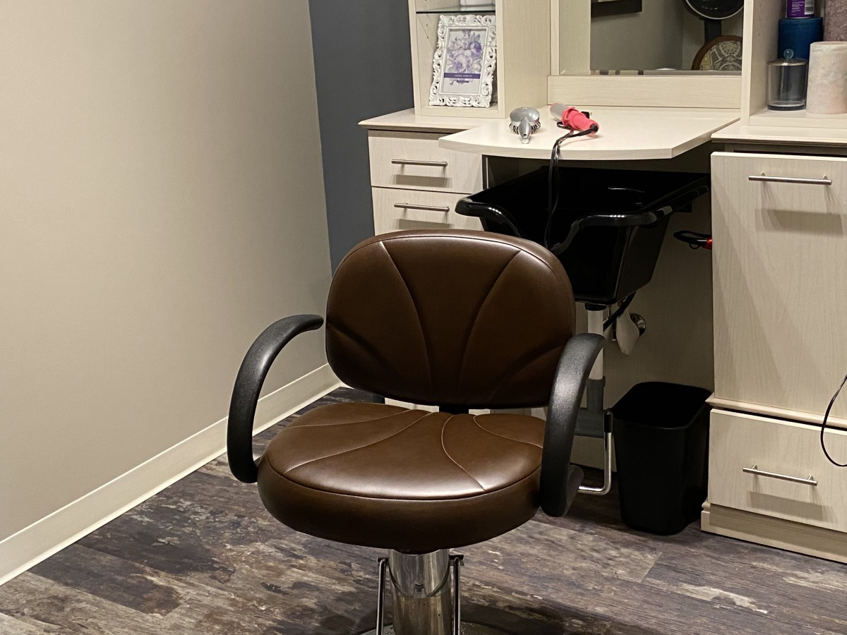 A salon chair in front of a styling station, complete with a mirror and sink.