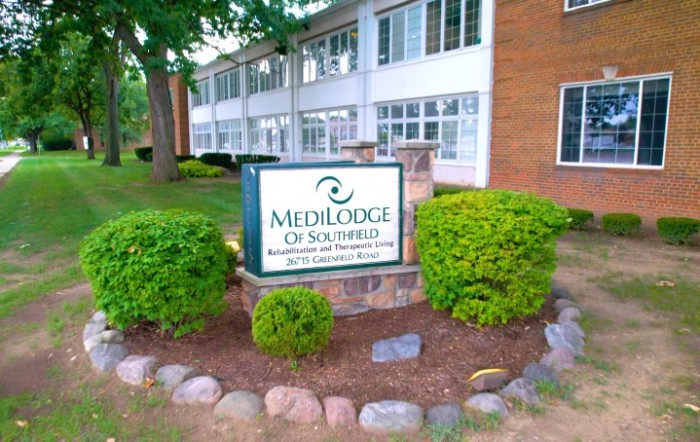 A nursing home building with a Medilodge sign surrounded by well-maintained landscaping.