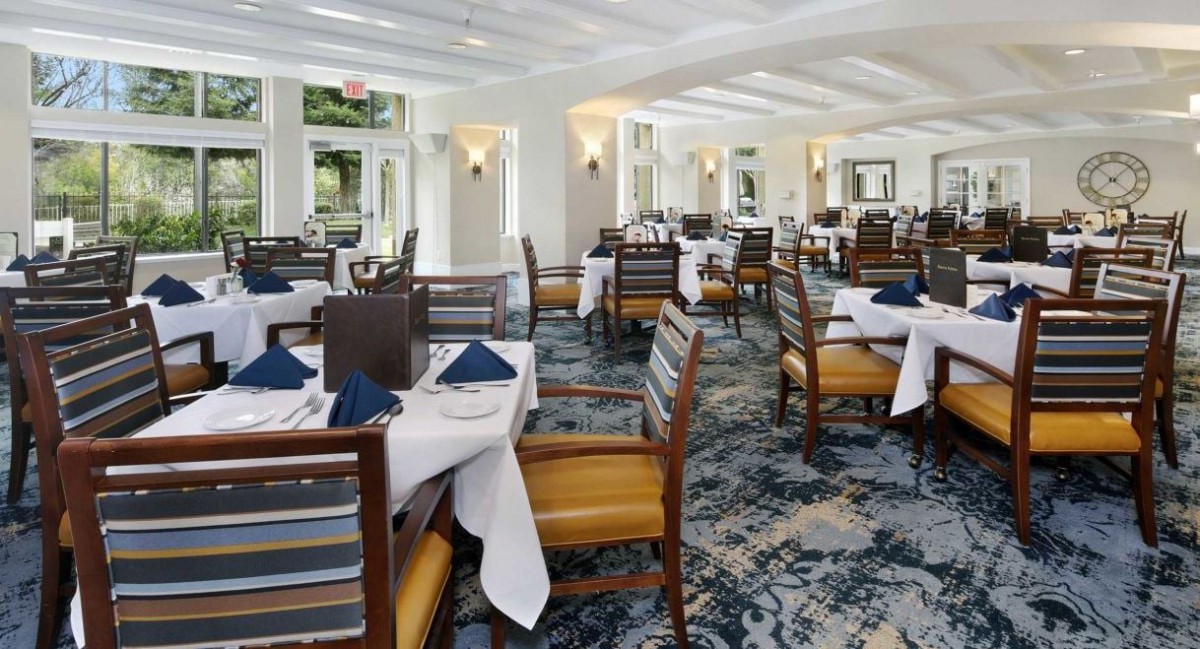 A spacious and elegantly designed restaurant dining area with neatly arranged tables and chairs, set with tableware.