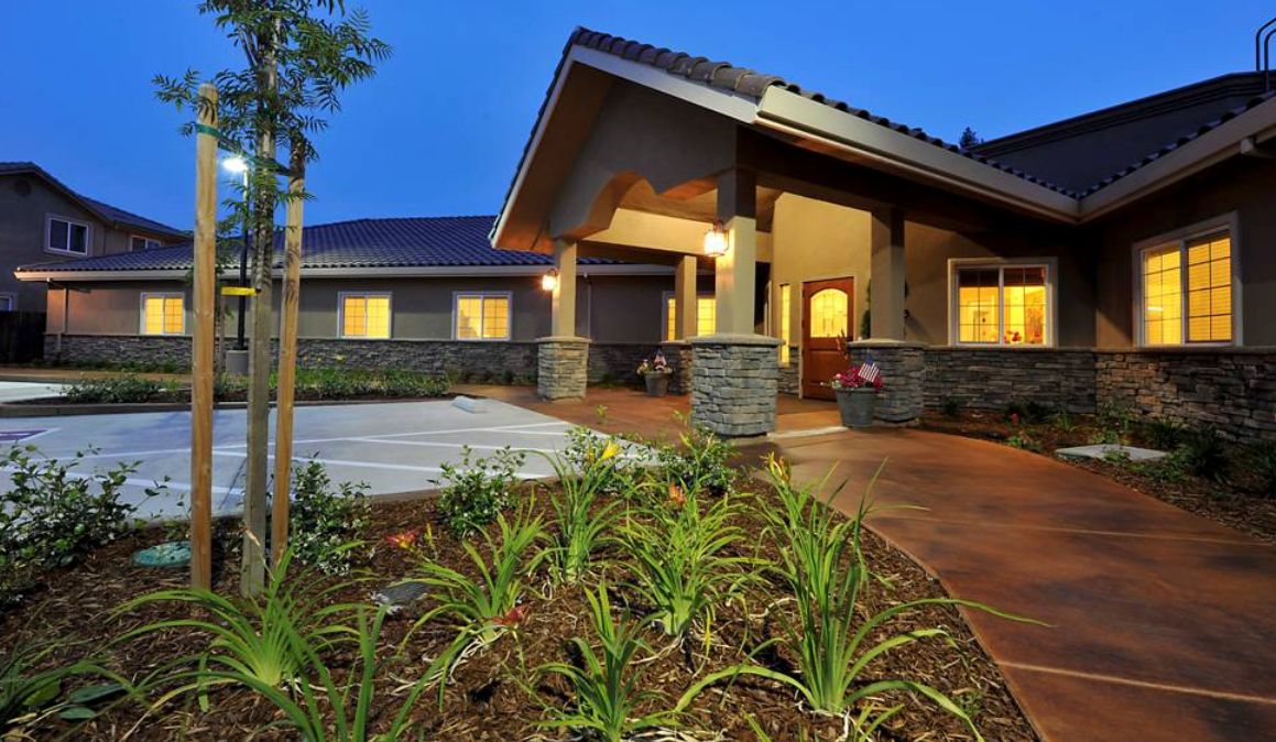 A modern residential house with illuminated exterior and landscaped garden in the evening.