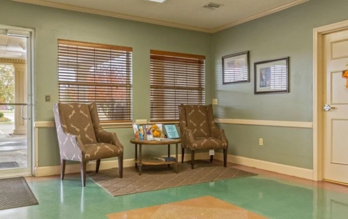 A cozy waiting room with two patterned chairs, a small table with decor items, and framed pictures on the walls.