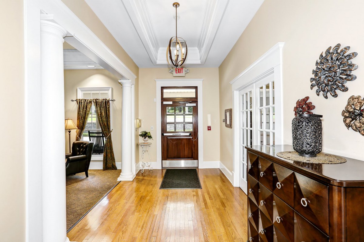 A bright and welcoming hallway with wooden flooring, a chandelier, and elegant decor.