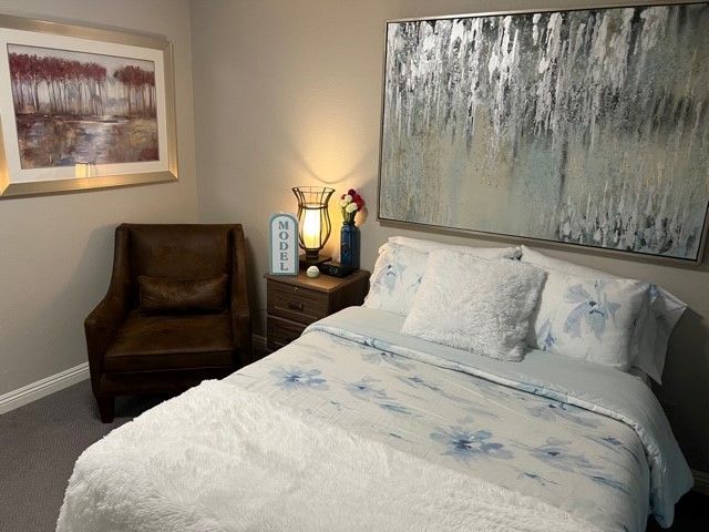 A cozy bedroom with a bed, decorative pillows, a painting on the wall, and a warm lamp.
