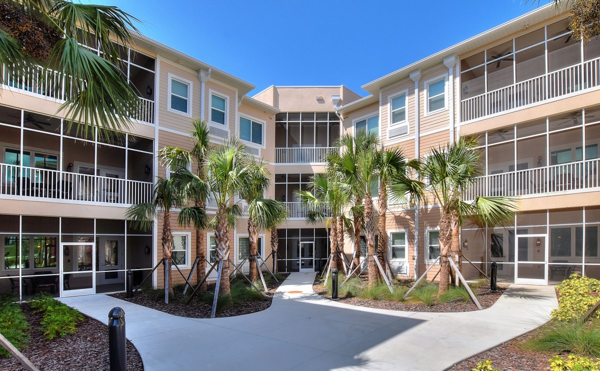 A modern apartment building surrounded by palm trees under a clear blue sky.