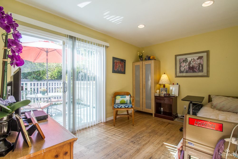 A cozy home office with wooden flooring and a sliding door leading to a patio, featuring a desk, chair, and ample natural light.