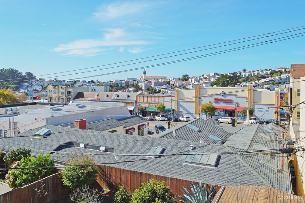 A view over the rooftops of a bustling urban neighborhood under a clear blue sky.
