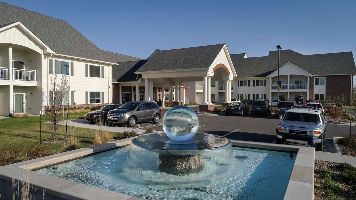 A modern hotel entrance with a prominent fountain feature and parked cars.