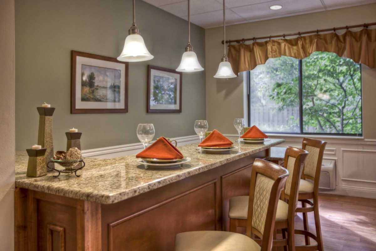 A cozy dining area with a bar counter, featuring pendant lights, framed artwork, and neatly arranged place settings.