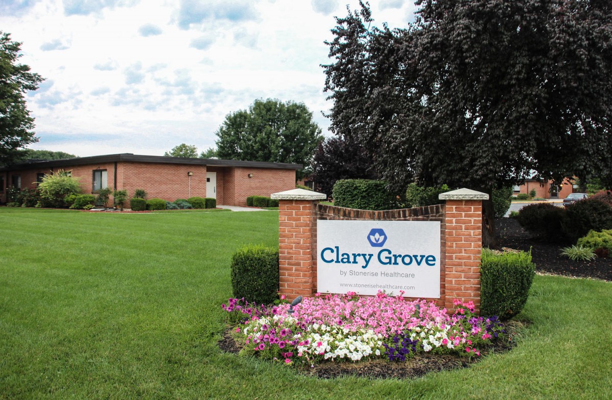 A landscaped area featuring a sign for Clary Grove, surrounded by flowers and greenery, with a building in the background.