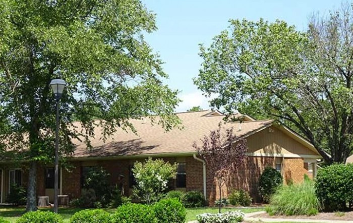 A suburban brick house surrounded by lush trees and well-maintained landscaping.