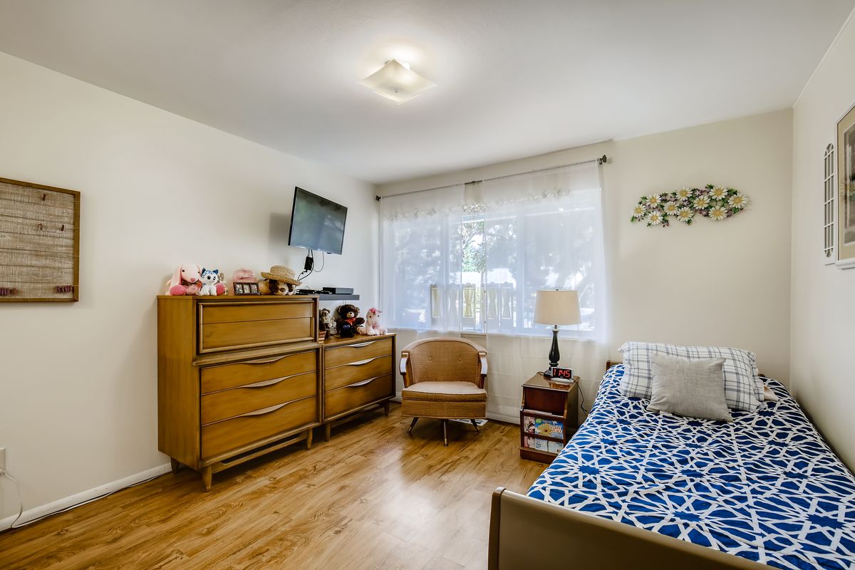 A cozy bedroom featuring a dresser, wall-mounted television, and a single bed against the wall.