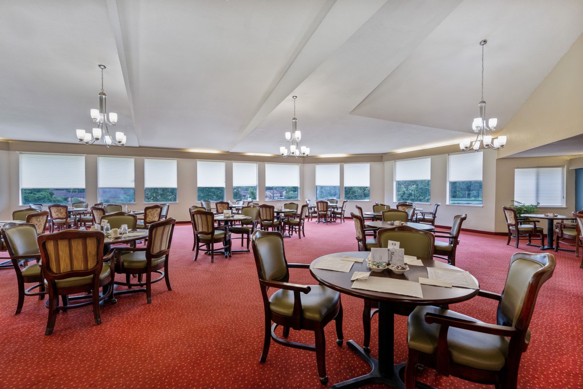 A spacious dining room with multiple tables and chairs, featuring large windows and elegant lighting fixtures.