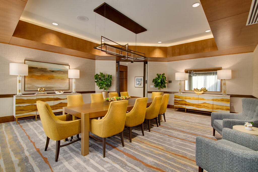 A modern dining room with yellow chairs and a wooden table, accentuated by artwork and indoor plants.
