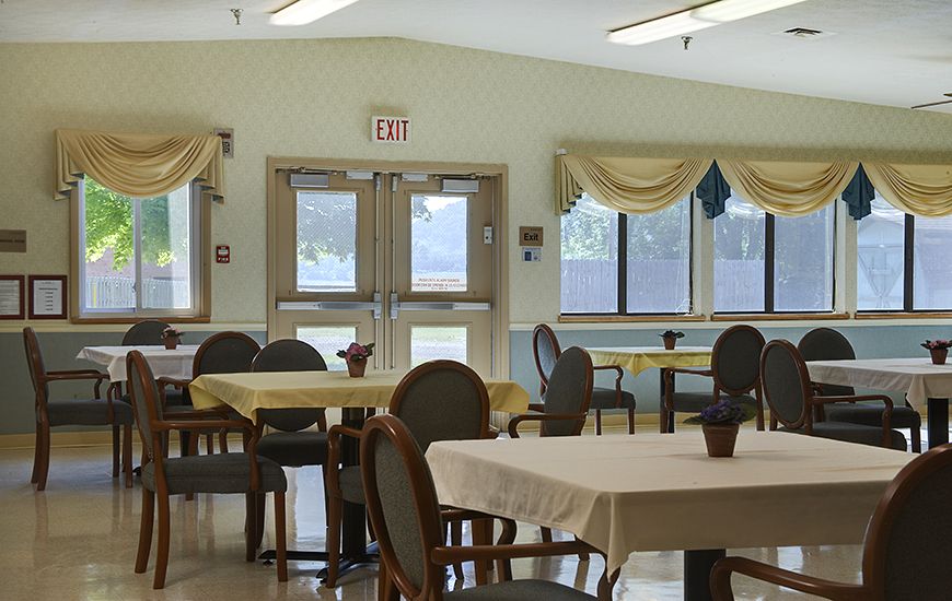 A well-lit dining room with tables and chairs, featuring large windows and natural lighting.