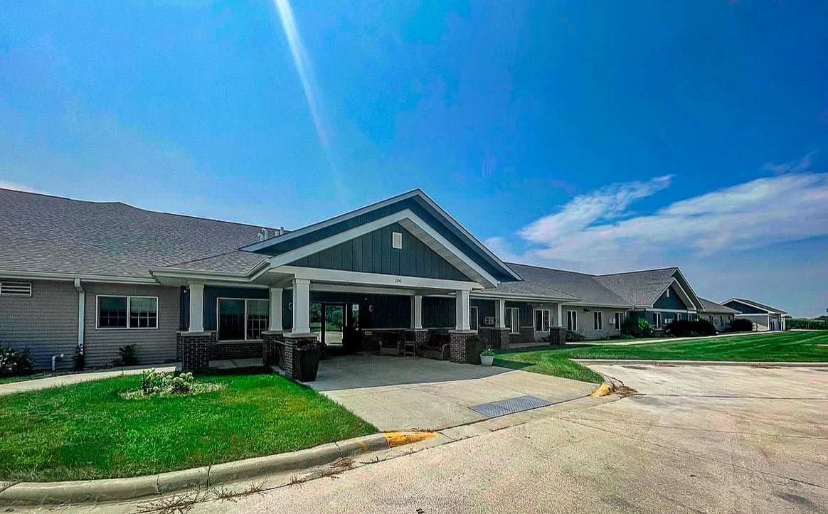 A modern residential building with a well-maintained lawn and driveway under a bright blue sky.