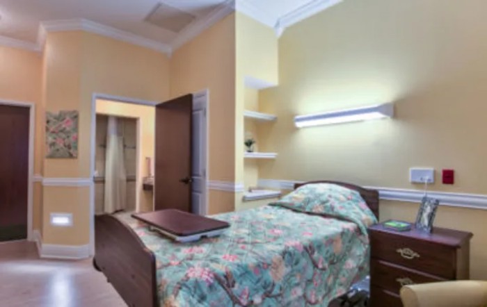 A cozy bedroom with a single bed featuring floral bedding, illuminated by a wall lamp beside an open door.