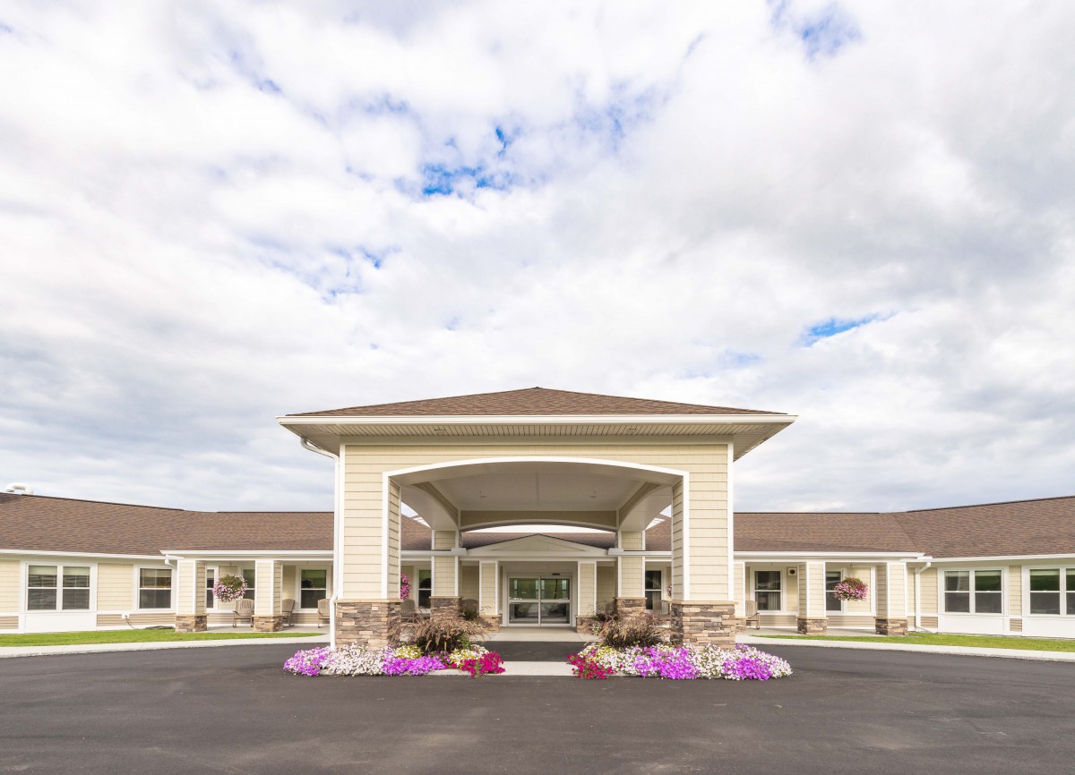 A scenic view of a building with a covered entrance and colorful flowers under a cloudy sky.
