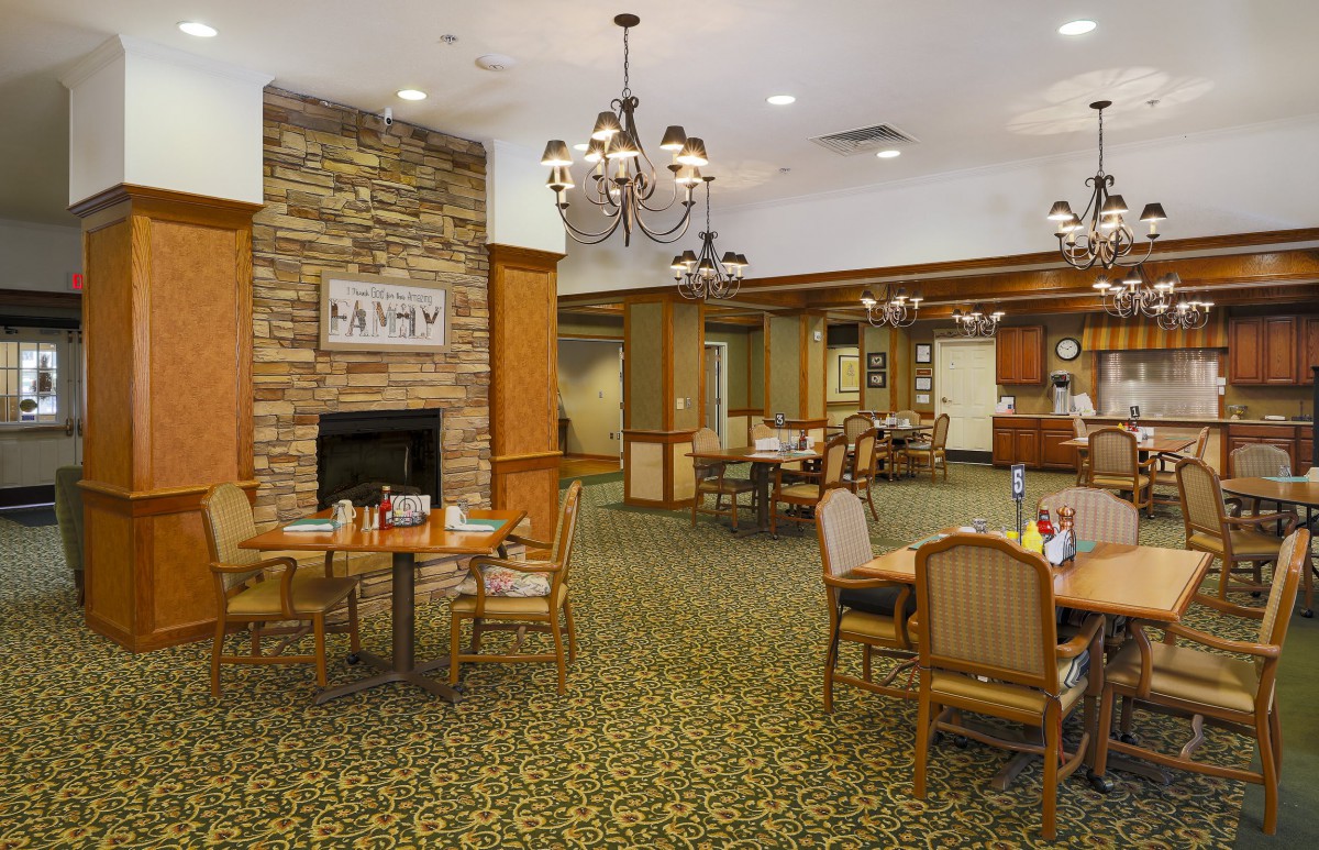 A cozy dining area featuring elegant chandeliers, a stone fireplace, and neatly arranged tables and chairs.