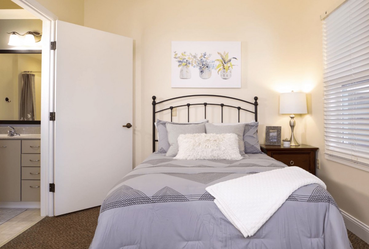 A cozy bedroom with a neatly made bed, a nightstand with a lamp, and decorative wall art above the headboard.