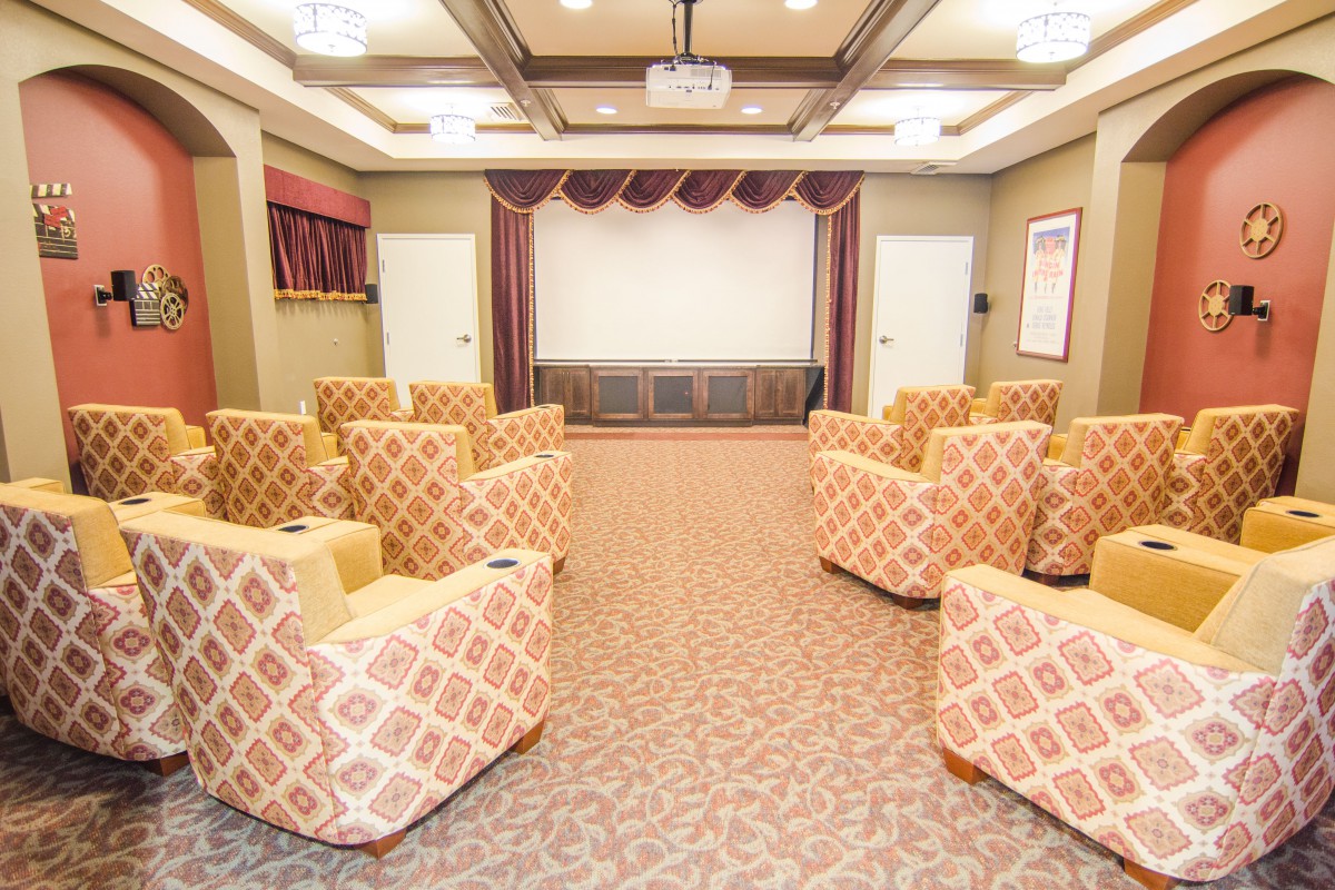 A cozy theater room with patterned armchairs arranged towards a large projector screen.