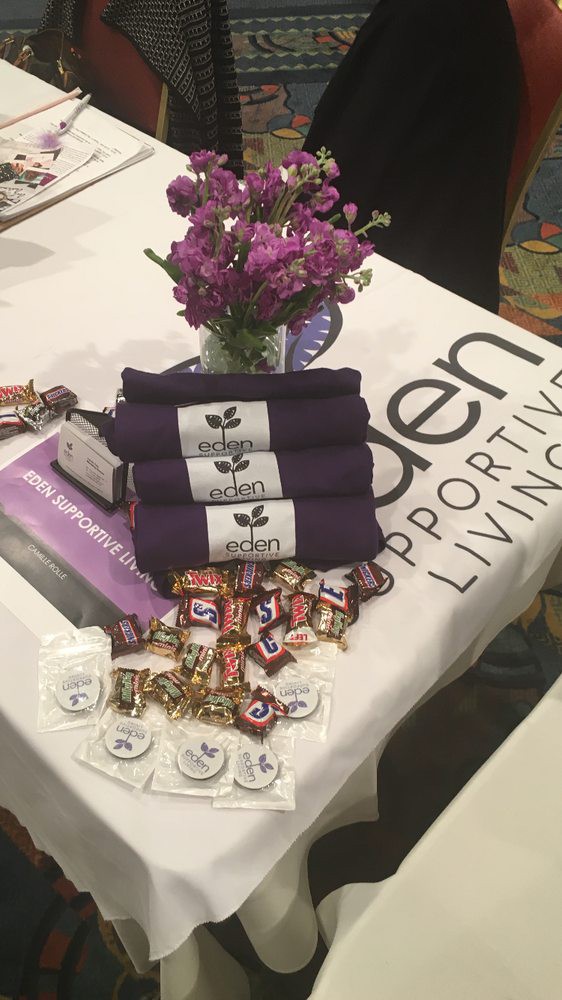 A display table featuring promotional towels, candies, and a flower arrangement at an event.