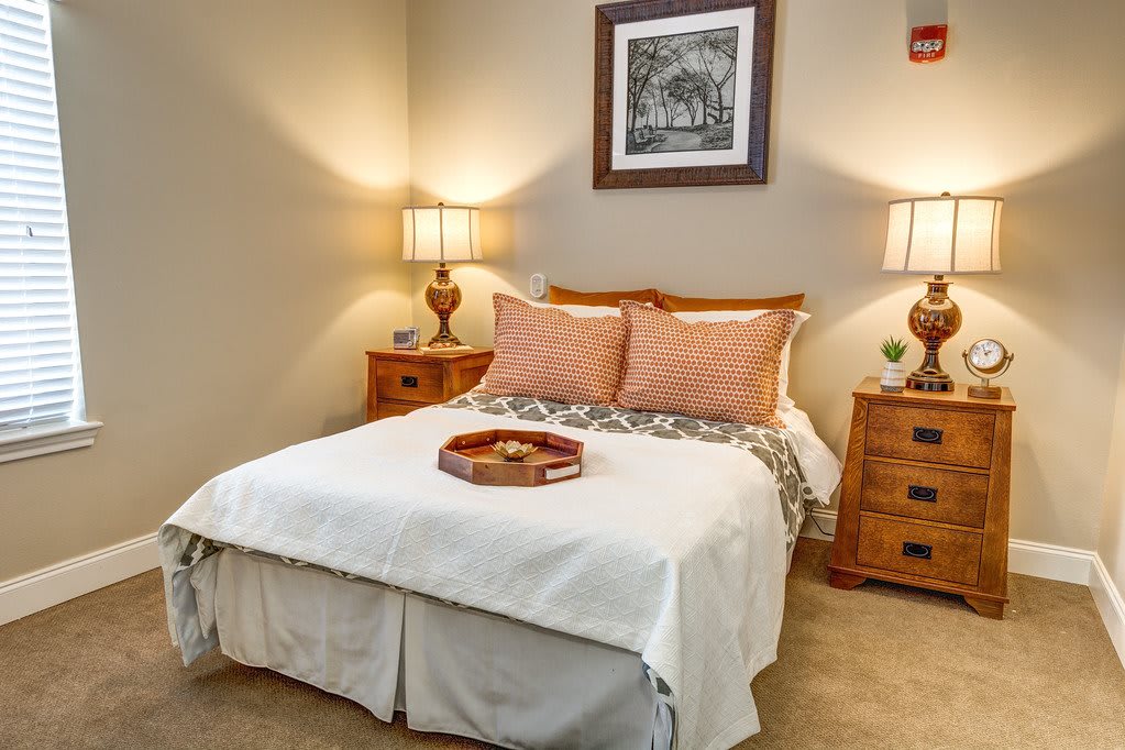A cozy bedroom with a neatly made bed and matching nightstands, illuminated by warm table lamps.
