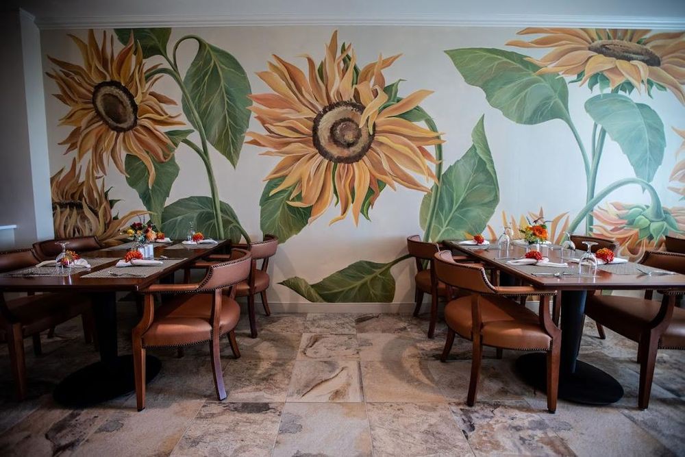 A cozy restaurant interior featuring a vibrant sunflower mural on the wall, with tables and chairs neatly arranged for dining.