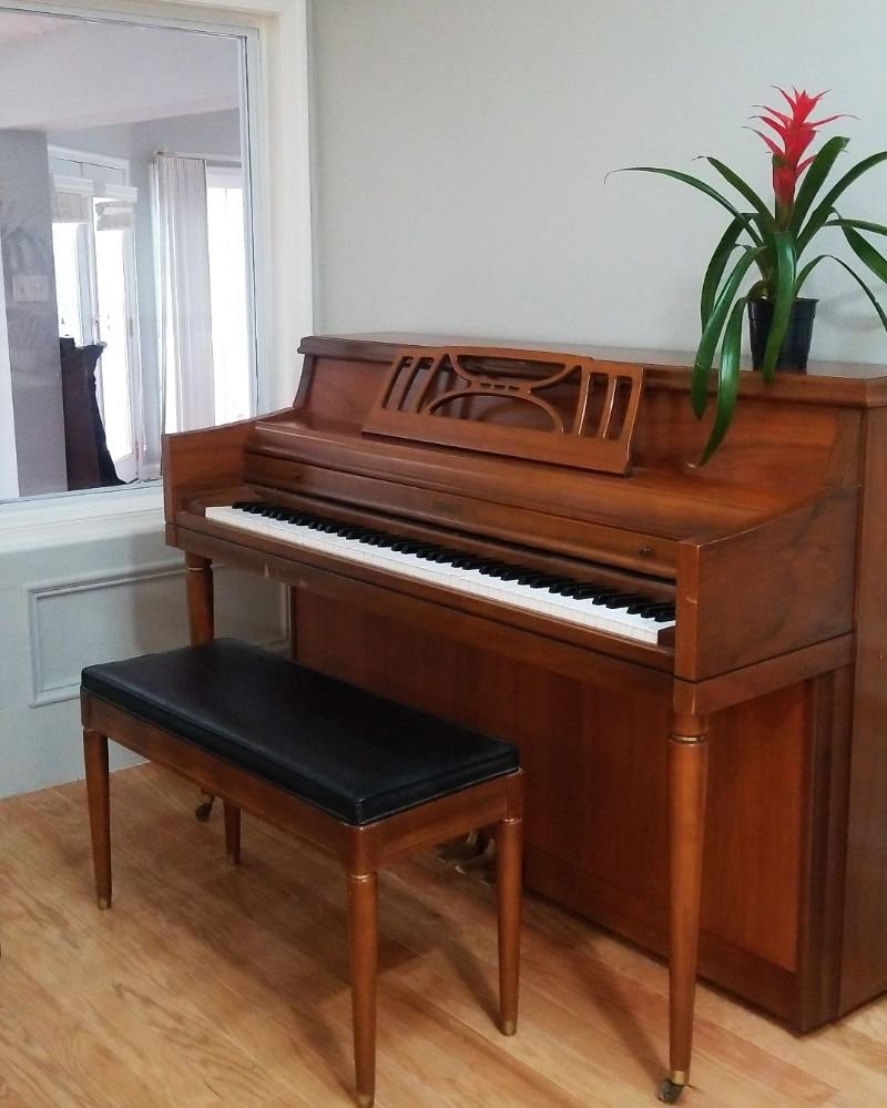 A wooden upright piano with a matching bench and a plant on top.