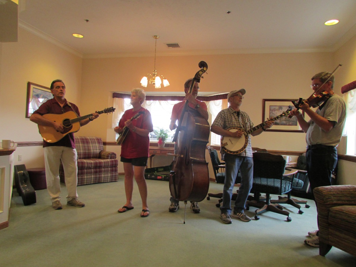 A band performing indoors with various instruments including a guitar, mandolin, double bass, banjo, and fiddle.