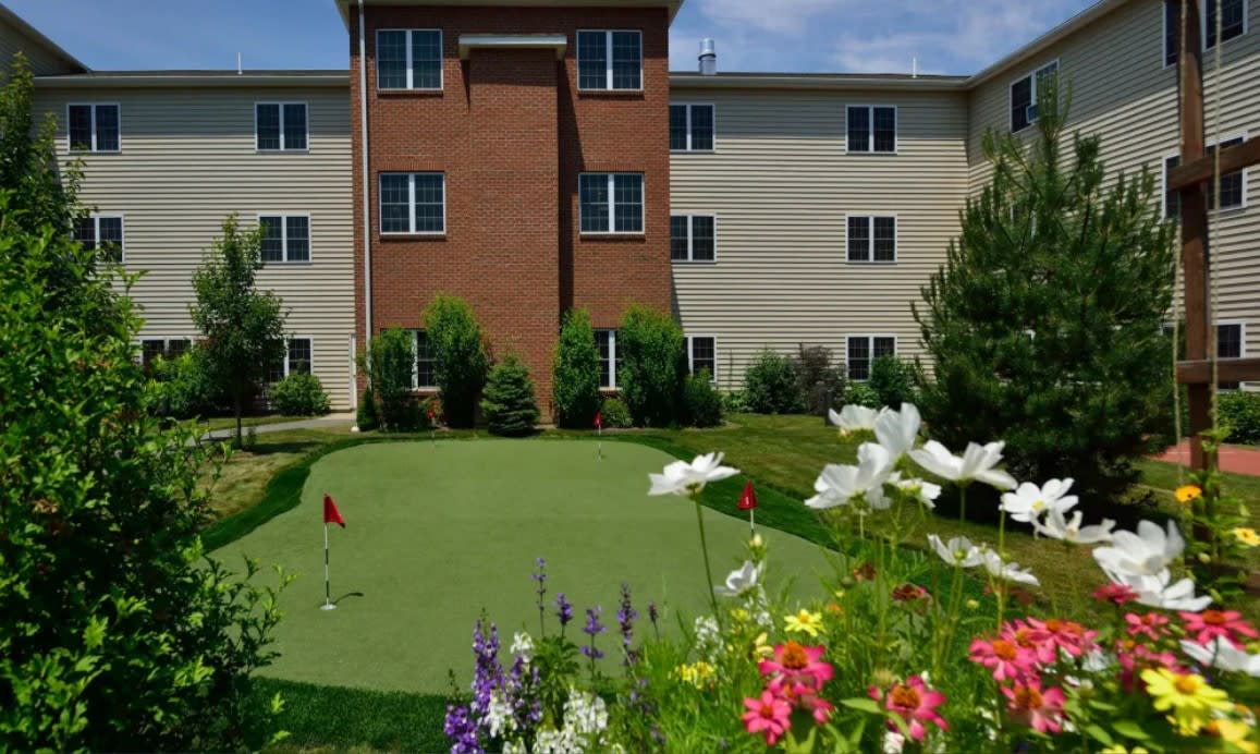 A residential building with a landscaped area featuring a small golf putting green and colorful flowers.