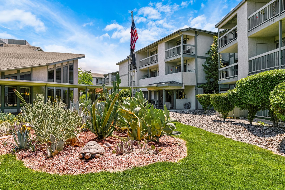 A sunny day at a landscaped apartment complex with a flag and well-maintained gardens.