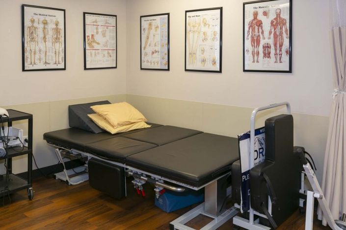 A physical therapy room with a massage table and anatomical charts on the walls.