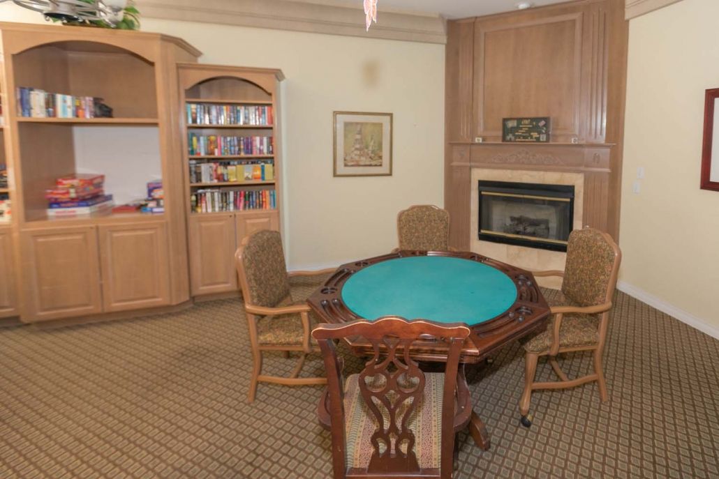 A cozy game room featuring a poker table surrounded by chairs, with a bookshelf and fireplace in the background.