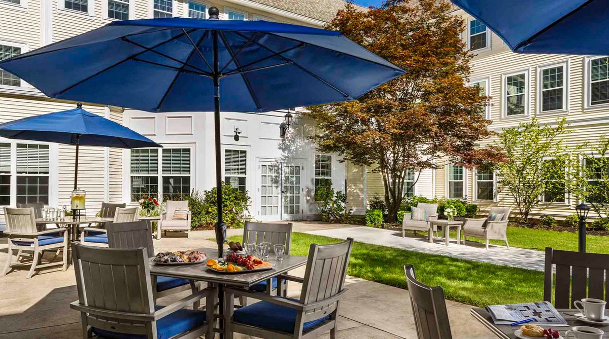 A sunny outdoor patio with blue umbrellas and garden furniture in a landscaped setting.