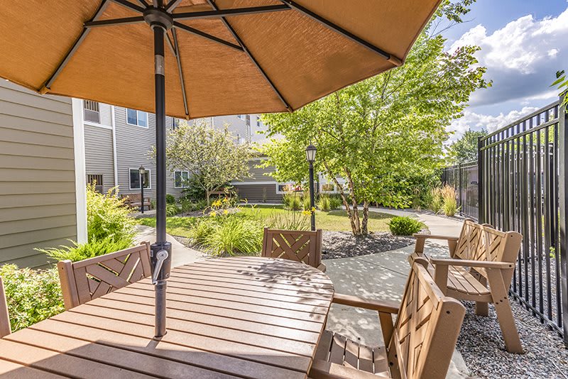 A sunny patio area featuring a wooden table with an umbrella, surrounded by lush garden landscaping.