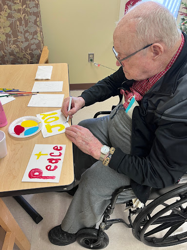 An elderly man enjoying a creative moment, painting colorful messages of peace at a table.