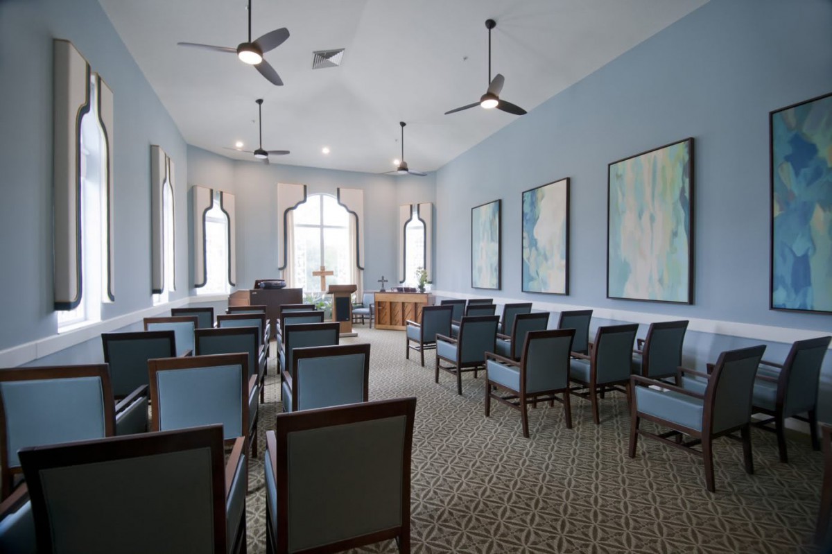 A peaceful chapel interior with rows of seating, large windows, and artwork on the walls.