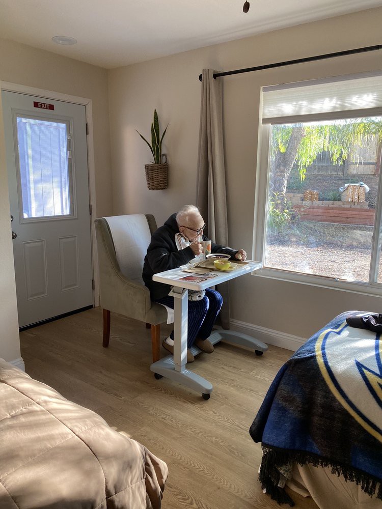 An elderly person enjoys a meal by the window in a sunny room.