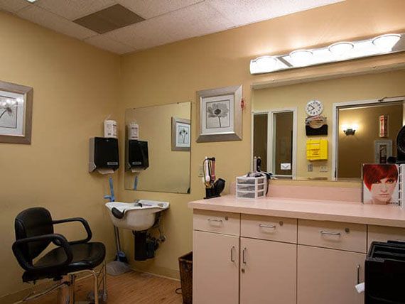 A makeup room with a large mirror, a chair, and a countertop featuring various items.