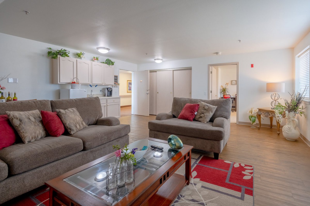A cozy living room with comfortable couches and a glass-top coffee table, featuring vibrant decor and greenery.