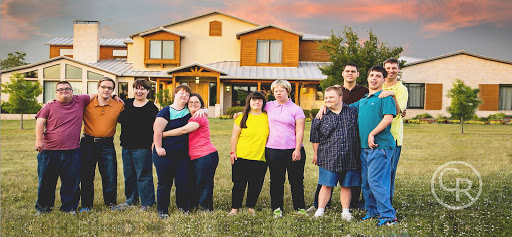 A joyful group of friends posing together in front of a beautiful home during sunset.