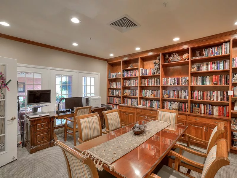 A cozy home library with wooden bookshelves and a central table surrounded by chairs.