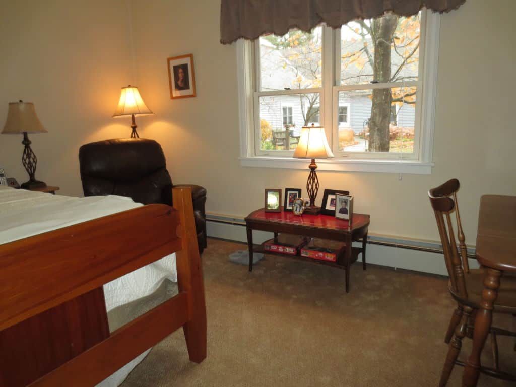 A cozy bedroom with a bed, armchair, and lamps by the window.