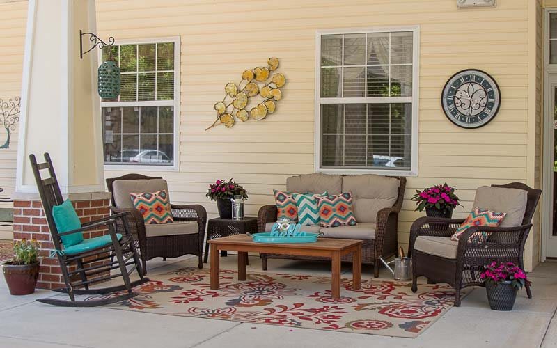 A cozy porch with comfortable patio furniture, decorative pillows, flower pots, and wall art.