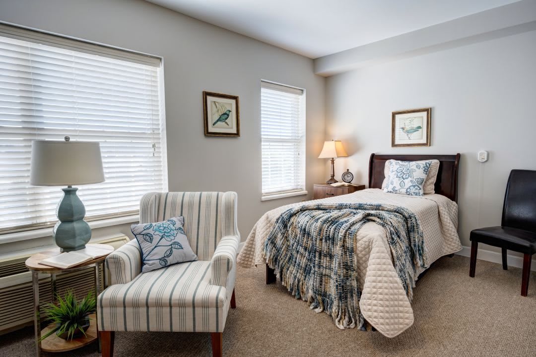 A cozy bedroom featuring a single bed, striped armchair, and soft lighting from a bedside lamp.