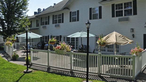 A view of a house with a patio area featuring umbrellas, outdoor seating, and a surrounding white fence.