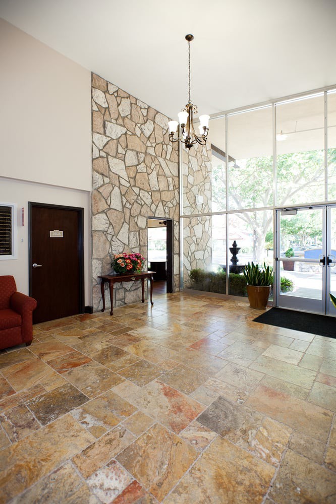 A spacious lobby with a stone wall, tiled flooring, and elegant furniture, leading to a glass entrance.