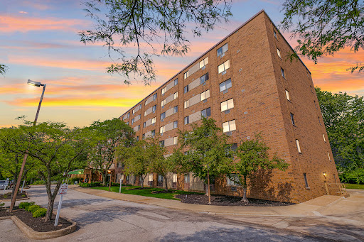 A modern brick apartment building illuminated by the warm glow of sunset, bordered by lush greenery.